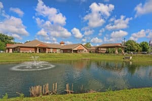 Front of facility with a large pond in front and water feature